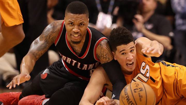 Damian Lillard y Devin Booker pugnan en el suelo por un balón.
