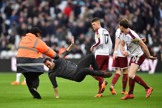 Burnley's English striker Ashley Barnes trips up a pitch invader during the English Premier League football match against West Ham United.
