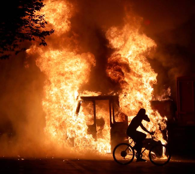 A man on a bike rides past a city truck on fire outside the Kenosha County Courthouse in Kenosha, Wisconsin, during protests following the police shooting of Jacob Blake.