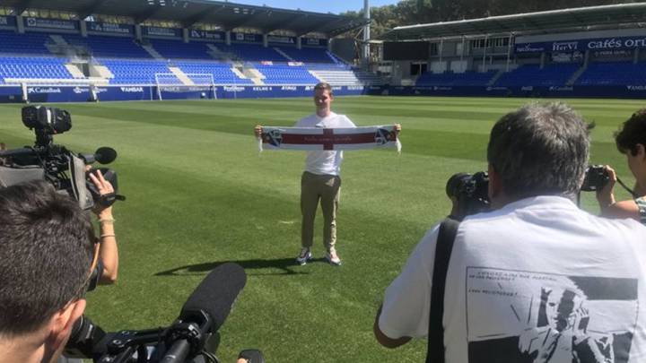 Sergio Gómez posa sobre el césped de El Alcoraz con una bufanda del Huesca (foto vía Twitter @SDHuesca).