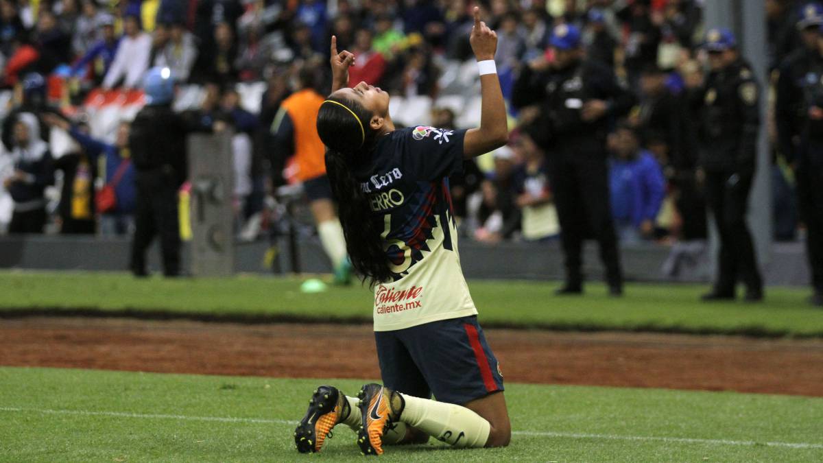 Jugadora de fútbol incada en el camopo de juego señalándo al cielo