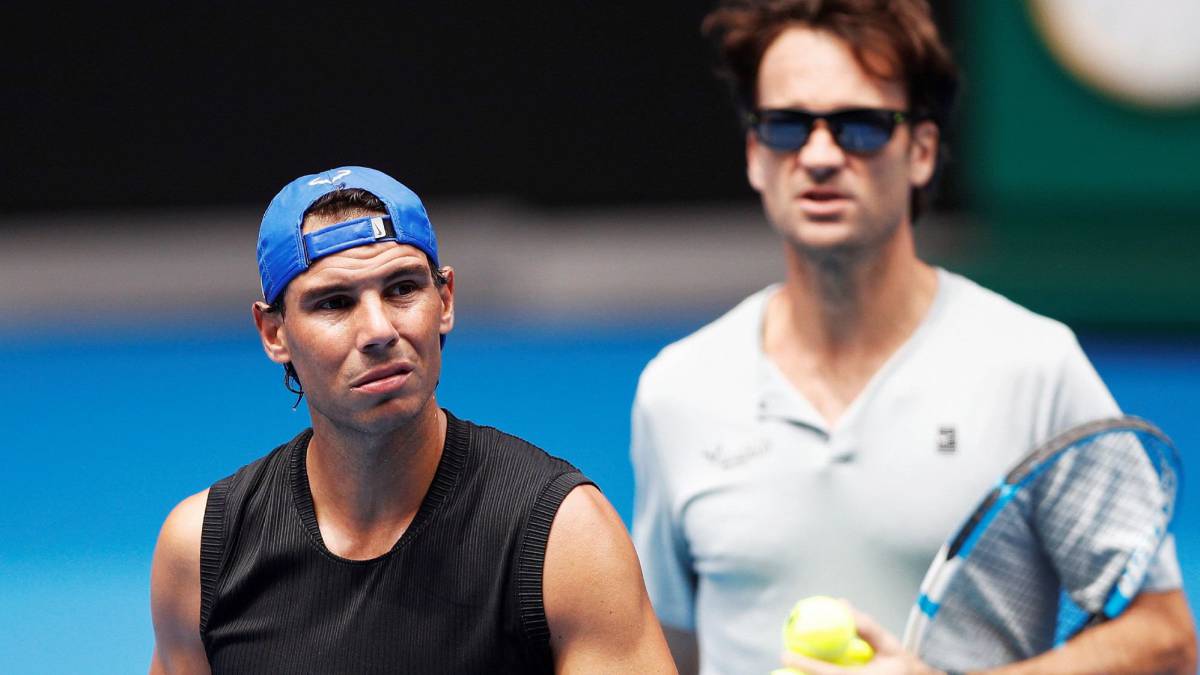 El tenista español Rafael Nadal (i) entrena en compañía de su entrenador Carlos Moya (d), en la pista Rod Laver Arena.