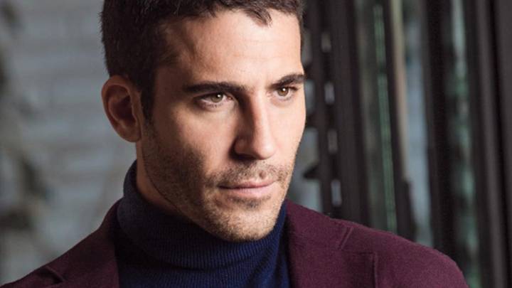 El actor Miguel Ángel Silvestre posa con un jersey azul y una americana burdeos.