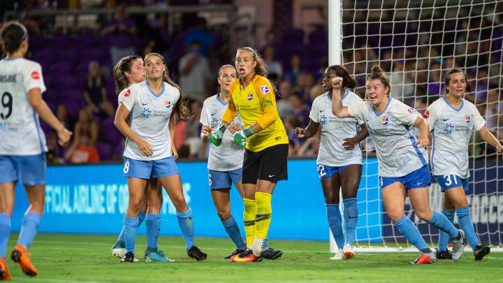 Jugadoras de fútbol femenil, vestidas con short azil cielo y playera blanca, además una de ellas hay portera con shor de color negro y playera amarilla.