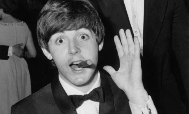 Paul McCartney saluda a la cámara con la mano izquierda mientras fuma un puto