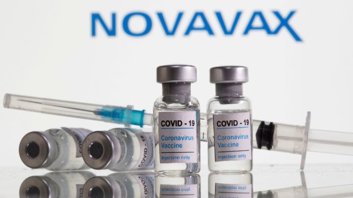 Viales etiquetados como "Vacuna contra el coronavirus COVID-19" y jeringa, Detrás, el logotipo de Novavax.