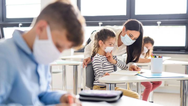 Niños y maestra usando mascarilla en salón de clases