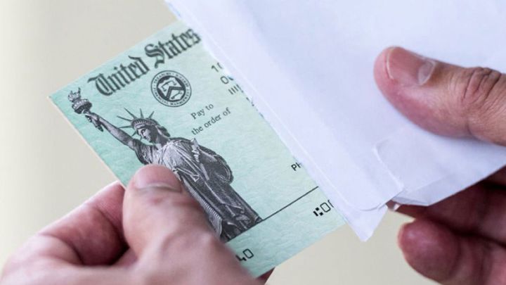 Mano sacando un cheque de estímulo de Estados Unidos de un sobre