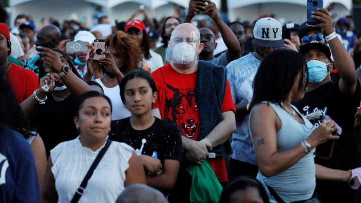 Una persona con mascarilla y careta entre una multitud sin mascarilla