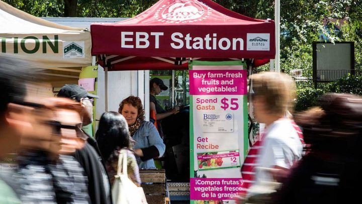 Personas caminando frente a una estación de alimentos que acepta la tarjeta EBT