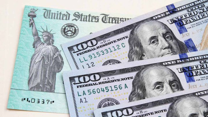 Cheque de estímulo estadounidense bajo billetes de 100 dólares estadounidenses