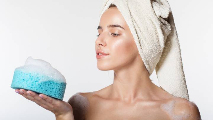Mujer joven recién salida de la ducha, con toalla en la cabeza y mirando esponja con restos de jabón