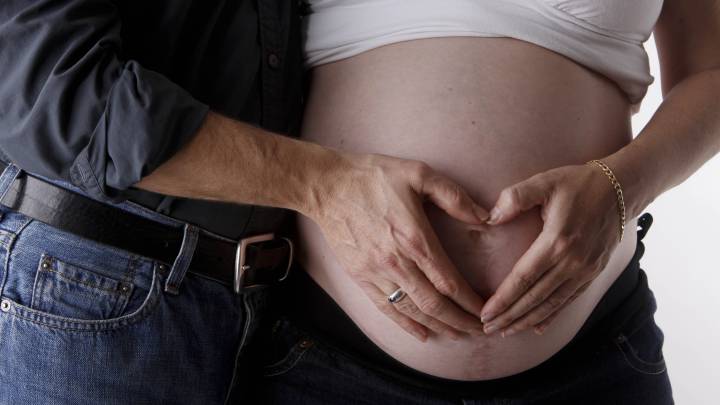 Una pareja, con una mujer angustiada, toca la barriga de la embarazada.