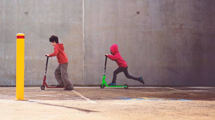 Dos niños juegan sin casco con patinetes eléctricos con el peligro de sufrir un golpe en la cabeza.