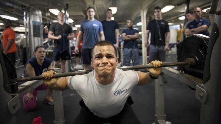 Un hombre hace ejercicio en el gimnasio ante la mirada de otros. 