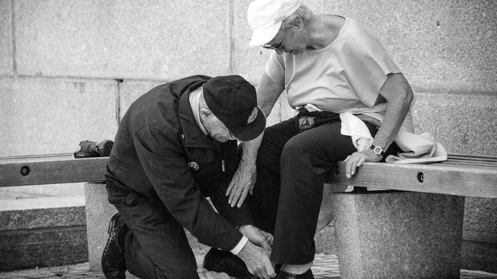 Un anciano ayuda a una anciana a atarse los zapatos. 