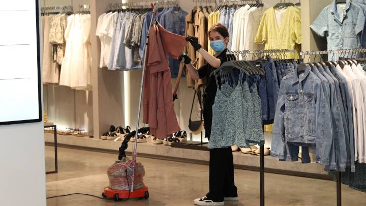Una dependienta desinfecta una prenda en el interior de una tienda en Madrid.