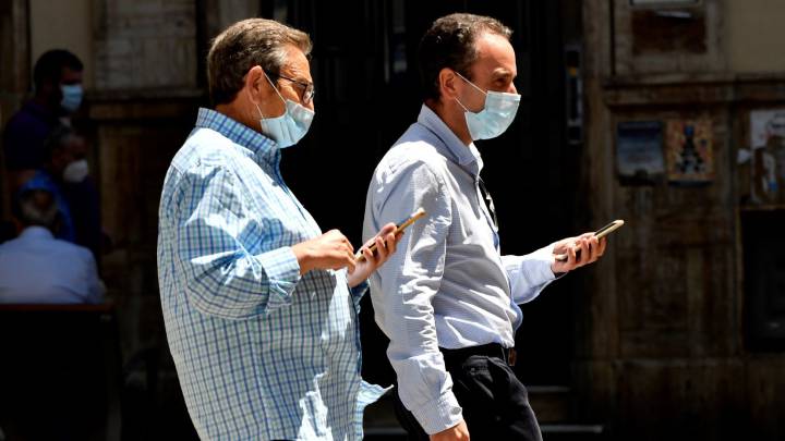 Dos hombres con mascarilla y móviles en mano pasean por una calle de Almería. 