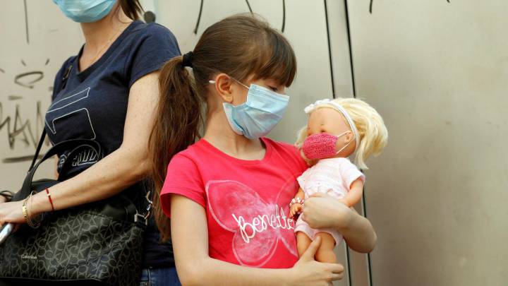 Una niña sostiene una muñeca a la que le ha colocado una mascarilla.