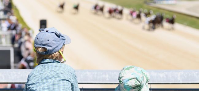 Dos niños ven carreras de caballos en sillas de montar en Addington Raceway (Nueva Zelanda).